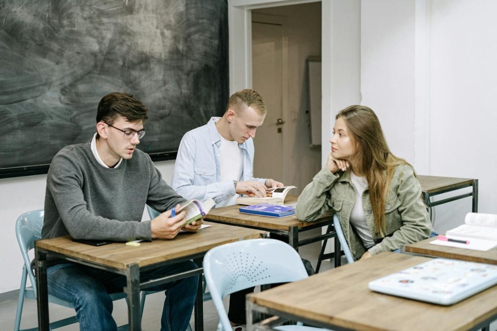 Group of young adults studying together in a classroom setting, engaged in reading and discussion.